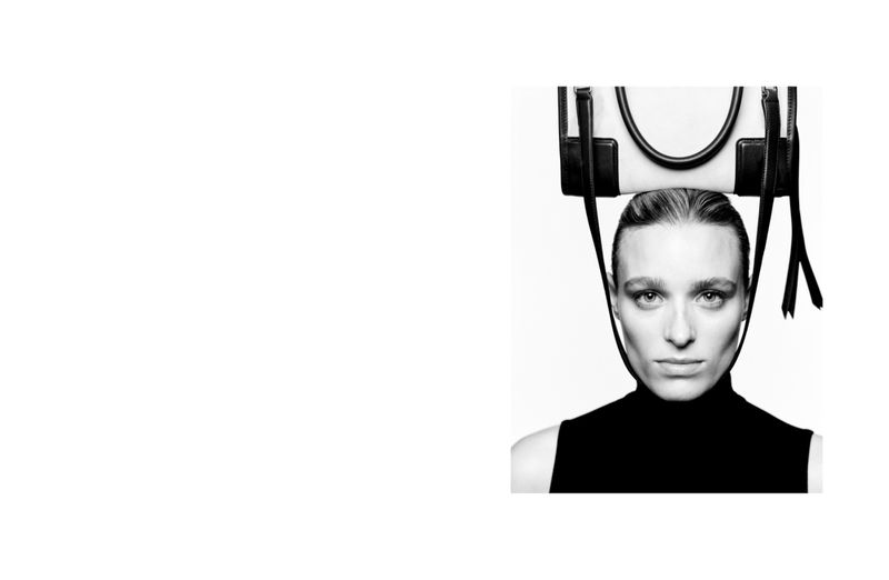 Close-up portrait of a model balancing a leather handbag on her head against a stark white background.