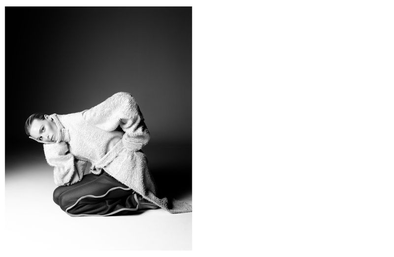 Model Katherine Wilkey crouching in a textured fleece coat and piped trousers in a monochrome studio portrait for At Large Magazine.