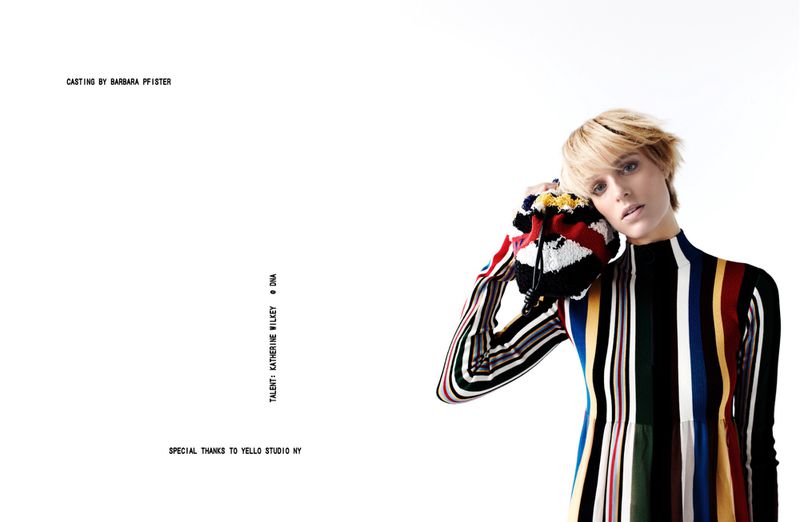 Katherine Wilkey posing in a multicoloured vertical striped knit dress with a textured drawstring bag against a white backdrop.