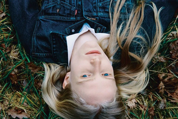 Model lying on grass wearing a dark denim jacket over a white collared shirt for Alei Journal x Levis editorial