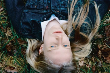 Model lying on grass wearing a dark denim jacket over a white collared shirt for Alei Journal x Levis editorial