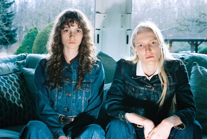 Two women seated on a sofa wearing matching denim jackets for an Alei Journal and Levis project, shot by Crista Leonard.