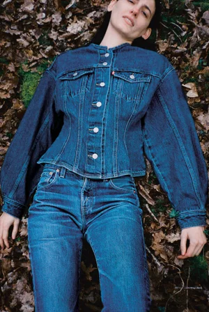 Model lying among fallen autumn leaves wearing a fitted denim jacket and blue jeans for Alei Journal x Levis