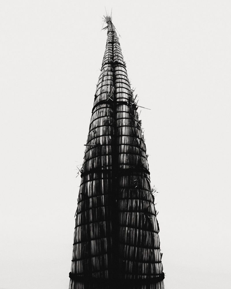 Monochrome photograph of an upright caballito de totora reed boat against an overcast white sky.