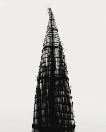 Monochrome photograph of an upright caballito de totora reed boat against an overcast white sky.