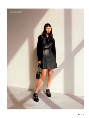Model Nicole Liew in a black leather dress holding a handbag against a wall with strong diagonal shadows for Elle Singapore