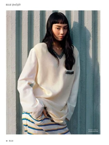 Model Nicole Liew in a cream knit vest and striped pants posing against a corrugated metal wall for Elle Singapore.