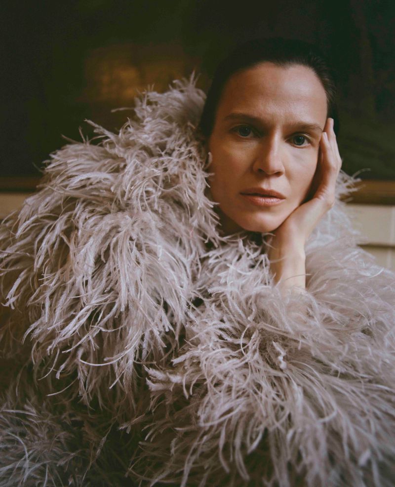 Model Santa Valentina wearing a voluminous grey feather coat, resting her head on her hand in a fashion editorial.
