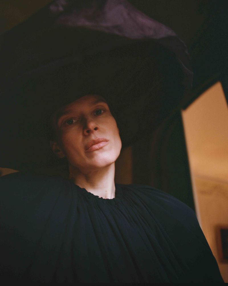 Model Santa Valentina wearing an oversized voluminous dark headpiece and gathered black garment in a low-angle portrait.