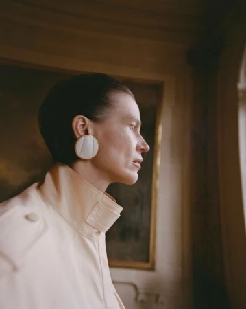 Profile portrait of a woman wearing a cream collar and large circular earring in an interior setting