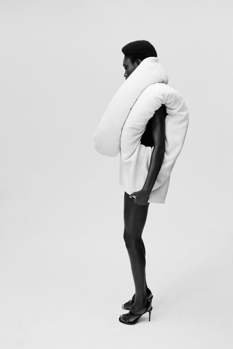 Model showcases white padded shawl with matching skirt and black heels in a studio shot with a clean white backdrop.