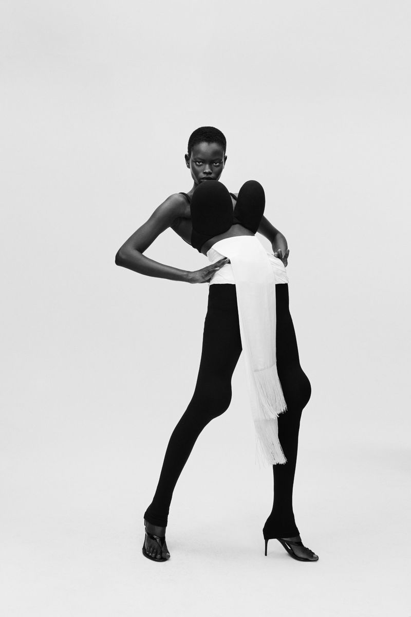 A striking black and white fashion shot of a slender black female model in hosiery and heels against a bright, neutral backdrop.