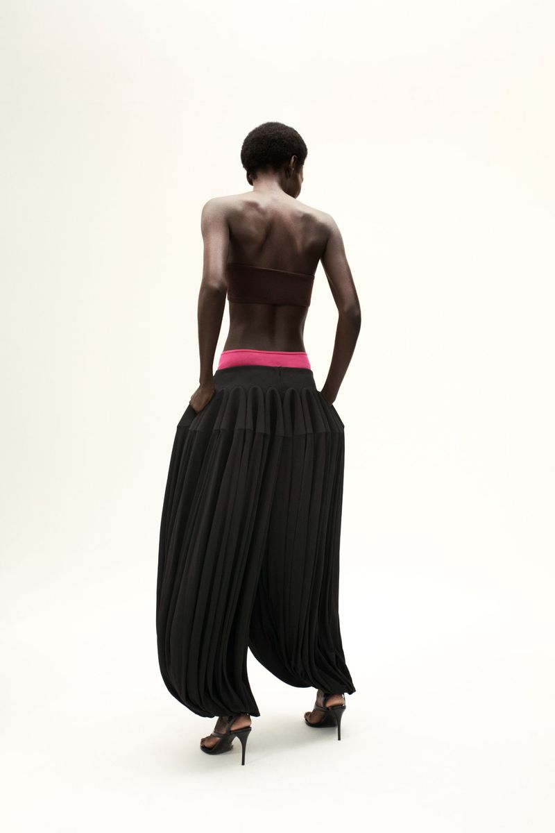 Back view of a Black woman wearing black culottes and high heels in a studio setting with neutral background. Fashion photography.
