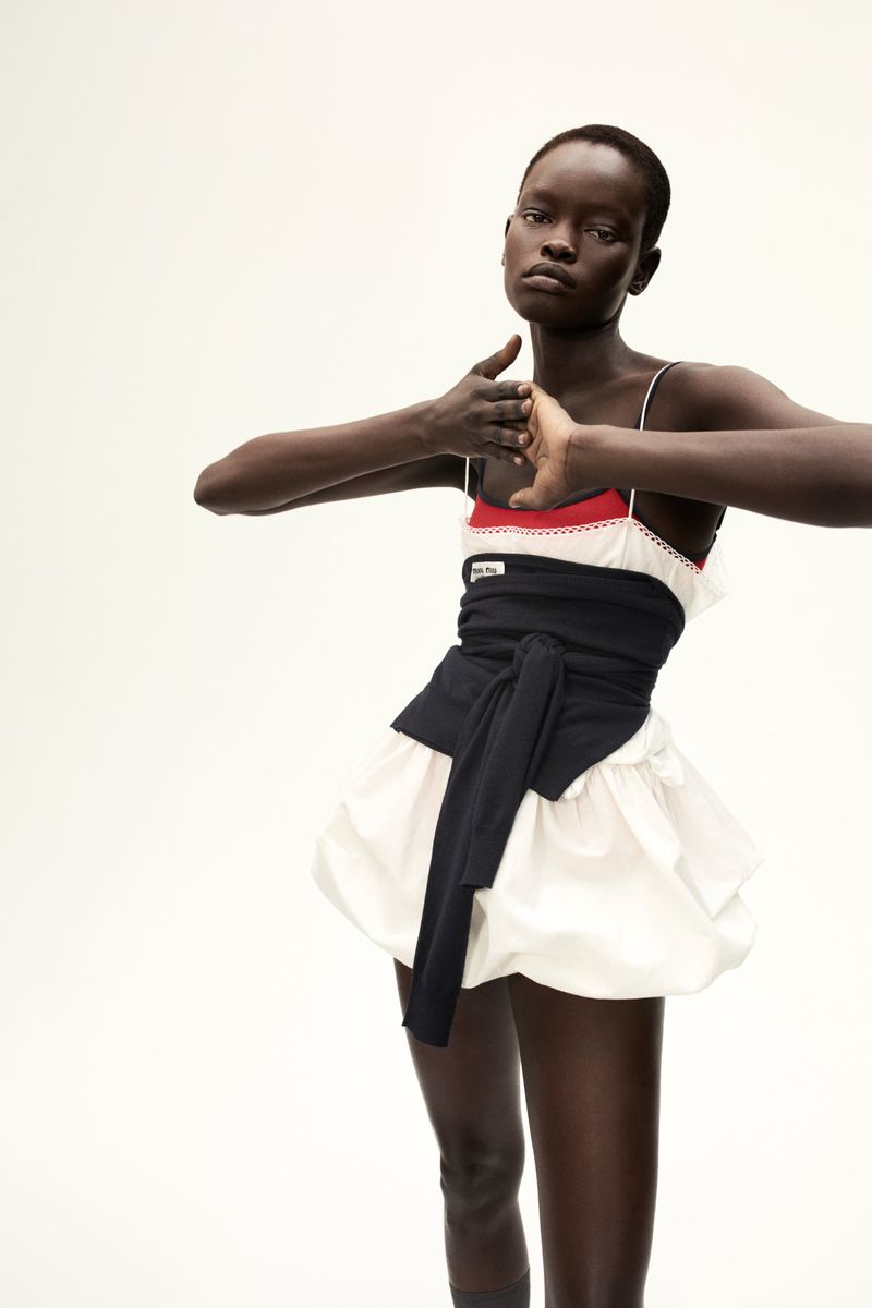Fashion shot of an African-descent woman in a white and red top with black obi-style belt and bubble skirt in a studio setting.