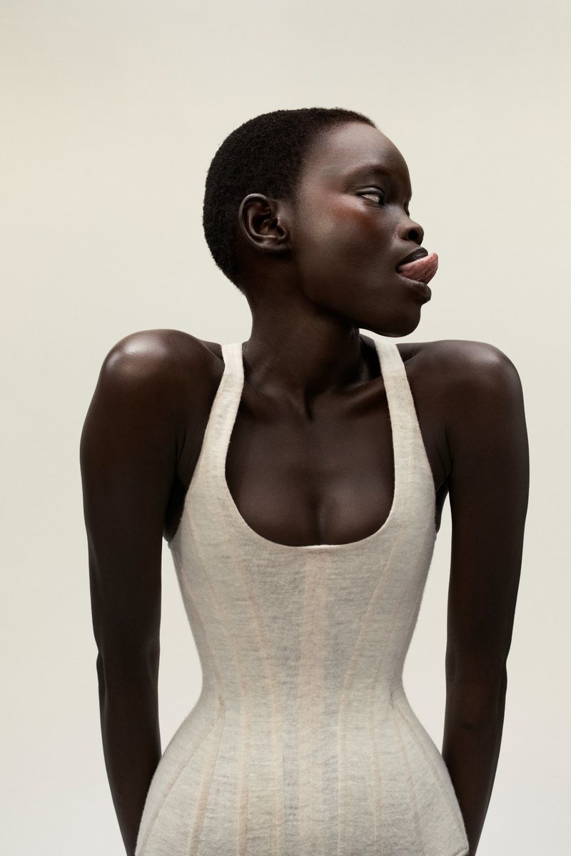 Portrait of a woman with dark skin and short hair wearing a light-colored top sticking her tongue out while looking to the side.