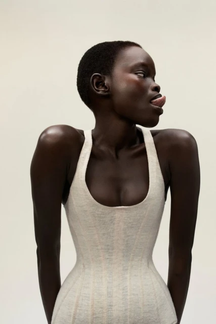 Portrait of a woman with dark skin and short hair wearing a light-colored top sticking her tongue out while looking to the side.