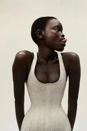 Portrait of a woman with dark skin and short hair wearing a light-colored top sticking her tongue out while looking to the side.