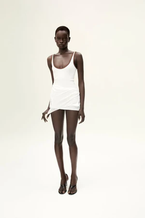 Model wearing a white dress standing against a plain white studio background