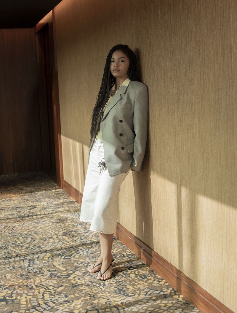 Model Sharon Alexie leaning against a textured hallway wall wearing an oversized sage blazer and white culottes.