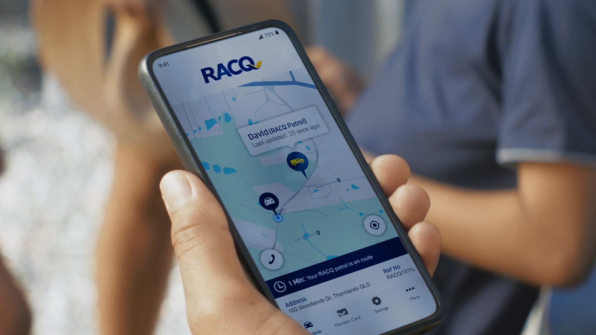 Person holding smartphone displaying a RACQ map with location pin, providing real-time roadside assistance and navigation information.
