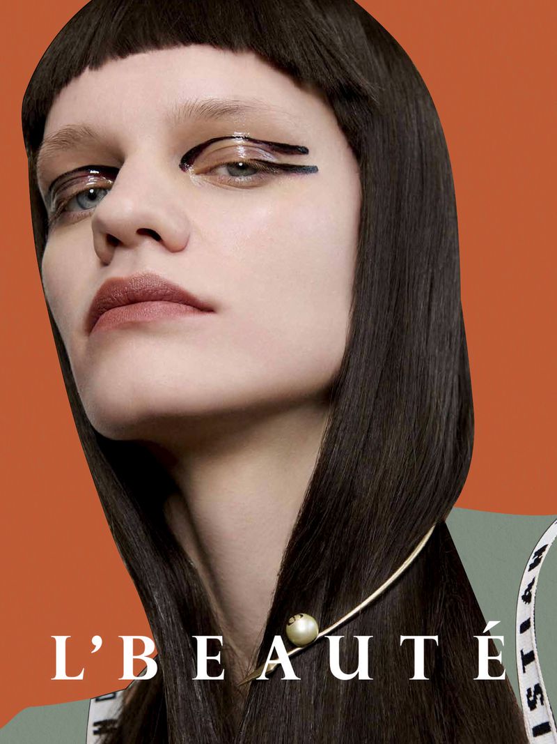 Close-up studio shot of a woman with dark hair and graphic black eyeliner against a vibrant orange background.