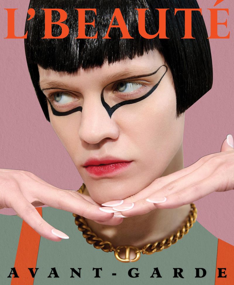 Beauty magazine cover featuring a model with bold graphic eyeliner, a gold necklace, and sleek black hair against a pink background.