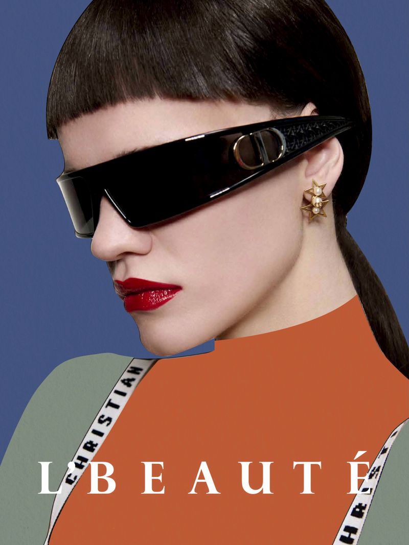A model showcases angular black sunglasses, red lipstick, and star-shaped earrings against a blue background in a close-up shot.