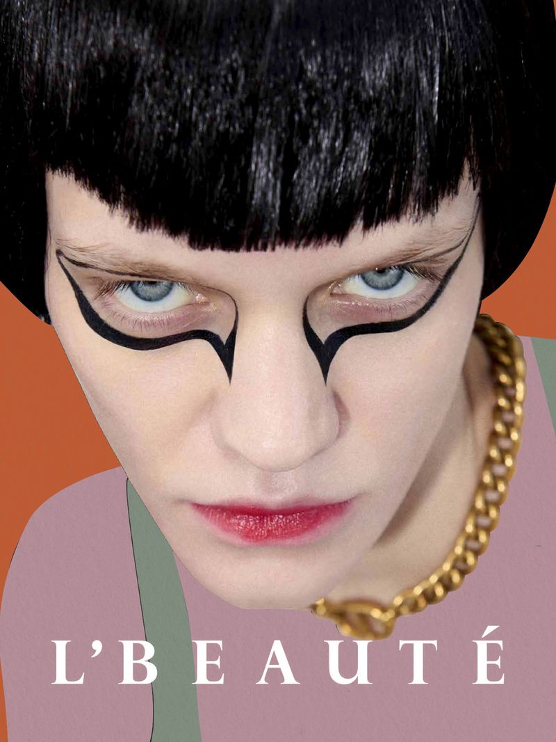 Close-up of a woman with bold black graphic eye makeup, short black hair, wearing a gold chain necklace, in a beauty advertisement.
