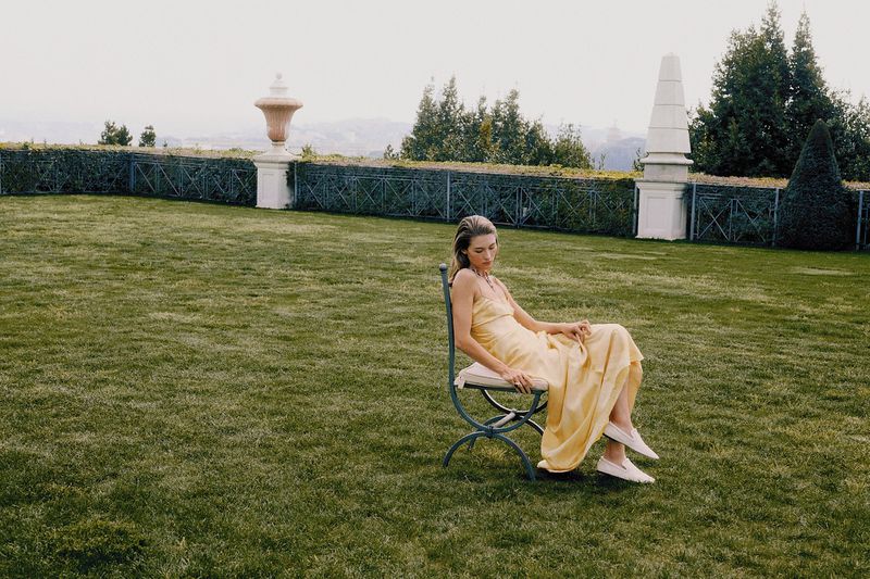 Grace Elizabeth in a yellow dress seated on a metal chair on a large green lawn for Vogue Turkey Cover Story editorial