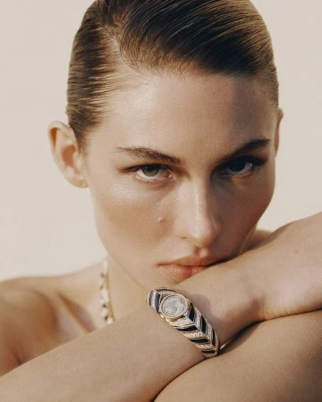 Close-up portrait of model Grace Elizabeth wearing a luxury watch with slicked-back hair against a neutral background.