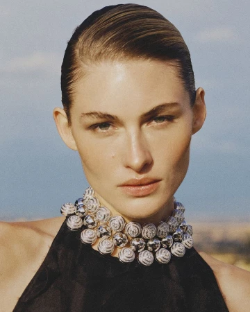 Close-up portrait of model Grace Elizabeth wearing an ornate spherical silver necklace and black halter top outdoors against a blue sky.