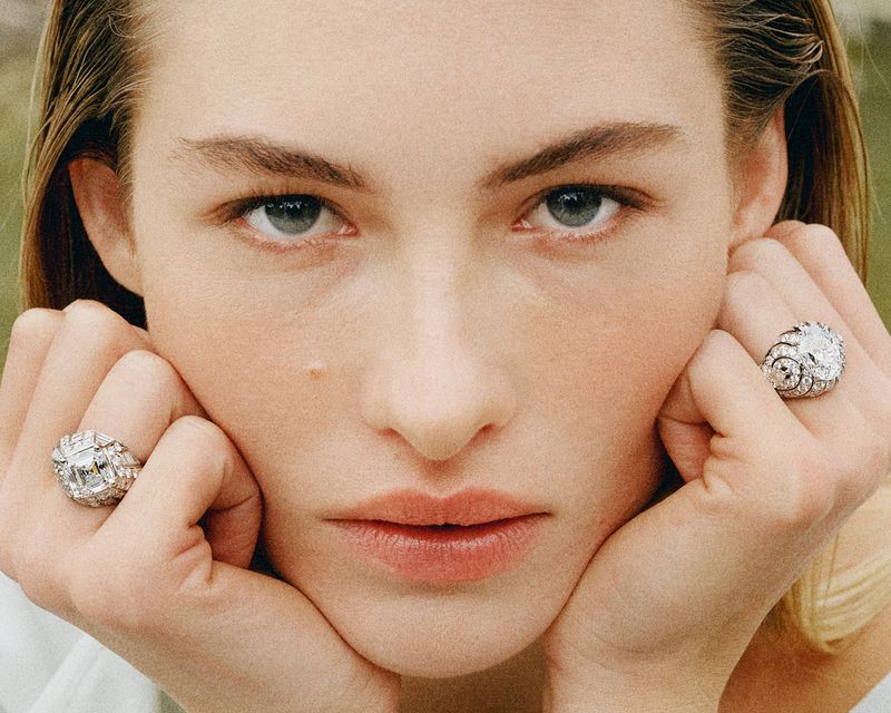 Model Grace Elizabeth resting her face in her hands while wearing large diamond rings in a close-up portrait.