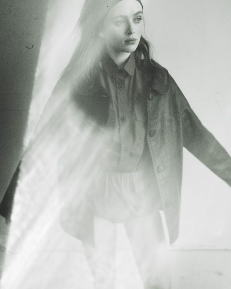 Sadie Sink posing in an oversized button-up jacket and shirt with soft light flare across the black and white frame.