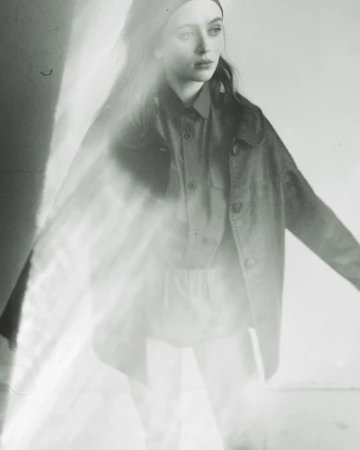 Sadie Sink posing in an oversized button-up jacket and shirt with soft light flare across the black and white frame.