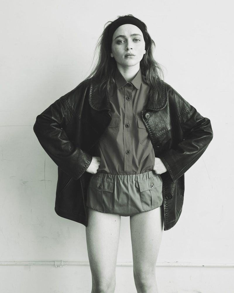 Sadie Sink wearing an oversized dark leather jacket and shorts against a plain wall for Pop Magazine