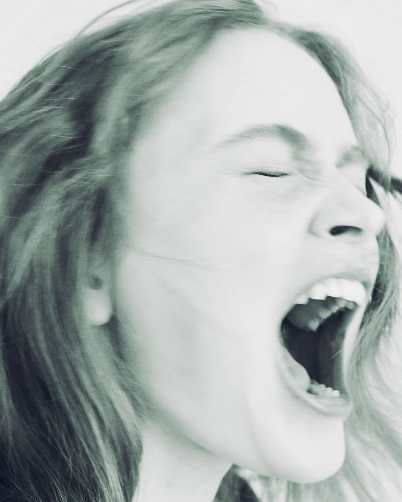 Close-up portrait of actor Sadie Sink screaming with mouth wide open against a pale background.