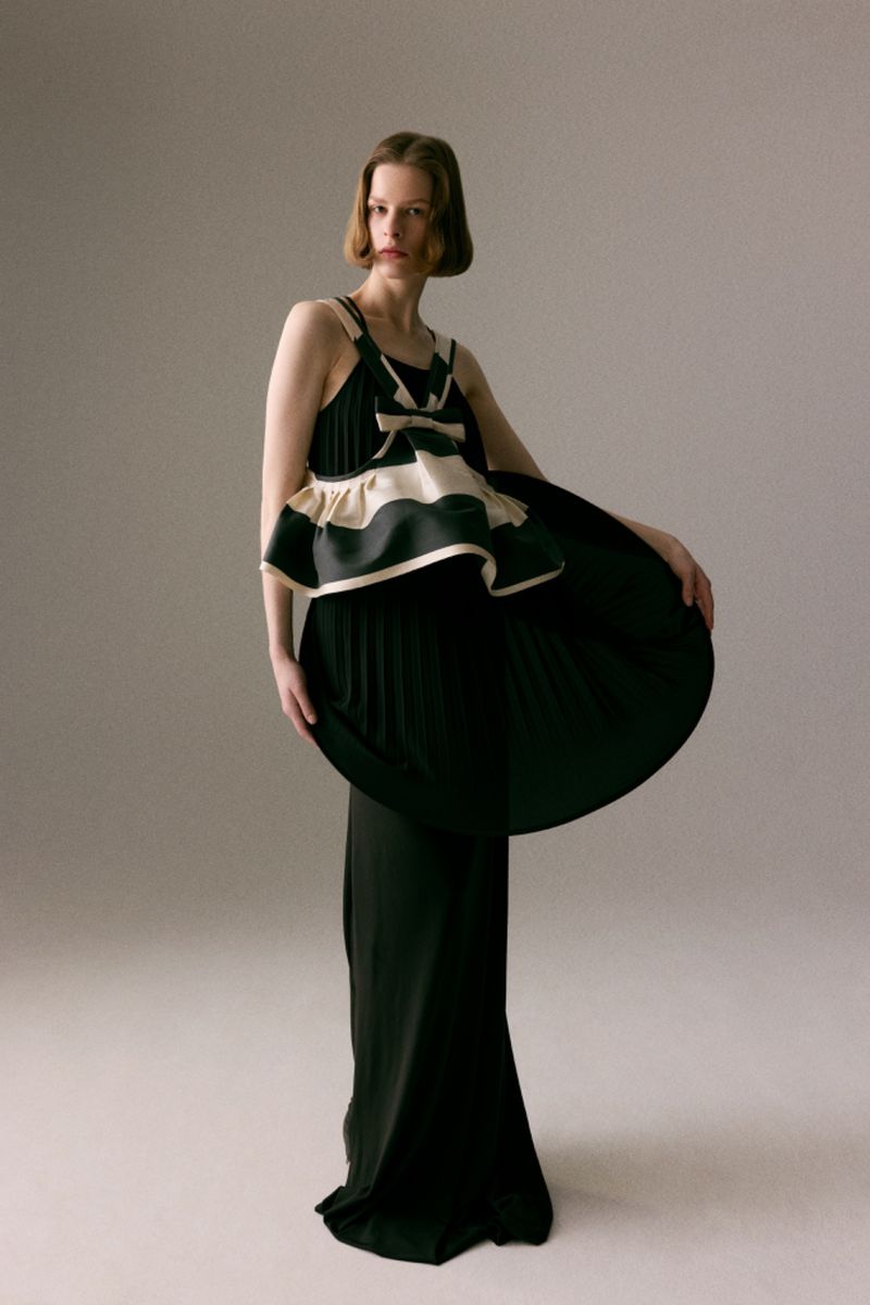 Model Hannah Weber poses in a floor-length black pleated gown with a sculptural cream-and-black top against a neutral studio backdrop.