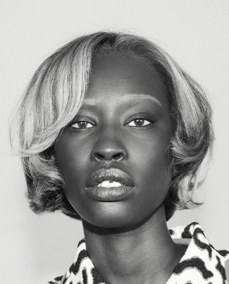 Close-up black and white portrait of a Black female model with short styled hair and bleached eyebrows in an editorial studio setting.