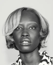 Close-up black and white portrait of a Black female model with short styled hair and bleached eyebrows in an editorial studio setting.