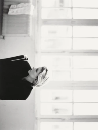 Black and white profile portrait of Camille Chifflot in a dark top with short blonde hair against a bright window.