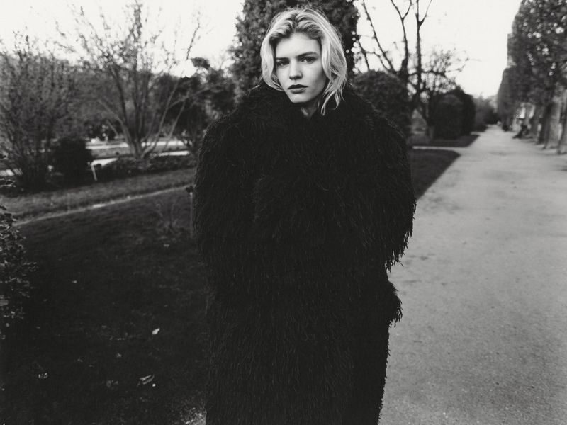 Model wearing a dark textured furry coat outdoors on a park path for Whatevr Magazine.