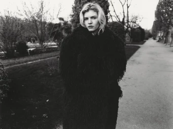 Model wearing a dark textured furry coat outdoors on a park path for Whatevr Magazine.