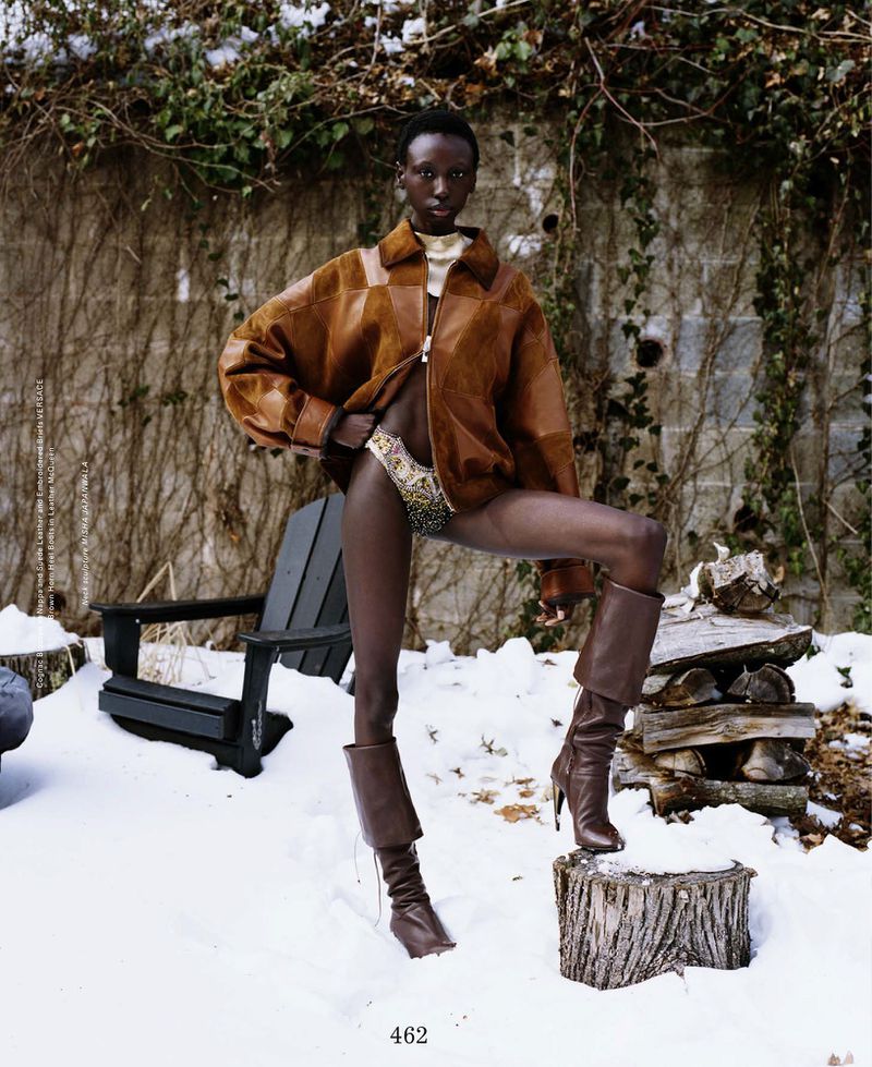 Model Alay Deng wearing an oversized brown leather jacket and high boots posing in the snow outdoors for ODDA Magazine.