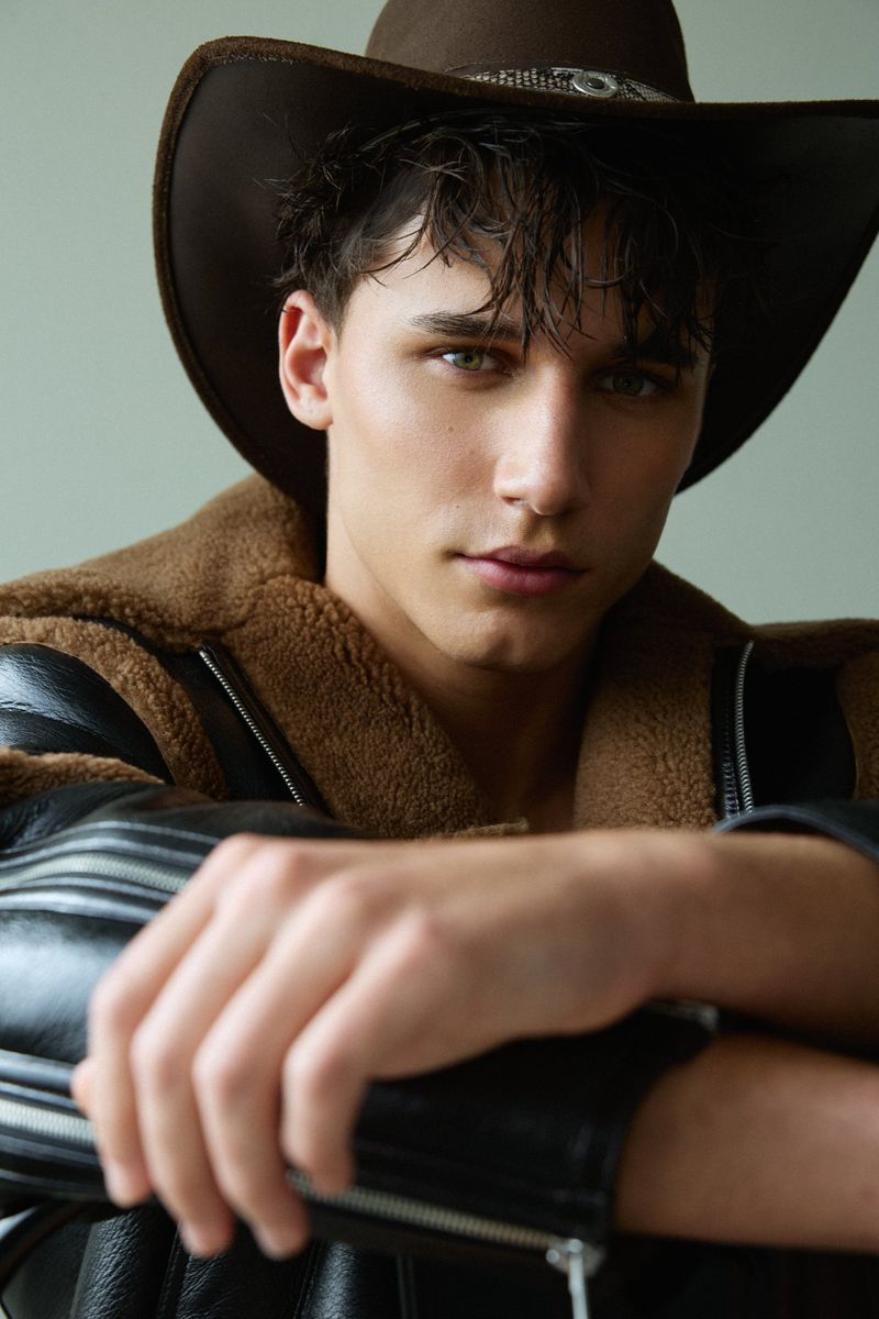 Close-up portrait of a male model wearing a brown cowboy hat and a black leather jacket with shearling trim.