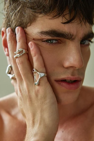 Close-up portrait of a man resting his hand on his cheek, wearing sculptural silver rings.