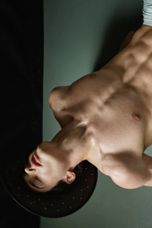 Shirtless male model wearing a dark studded cowboy hat leaning backward against a muted studio backdrop.