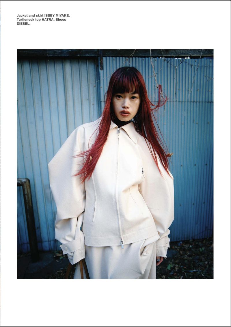 Model Yuki Beniya wearing an off-white sculptural zip jacket and skirt against a blue corrugated metal wall.