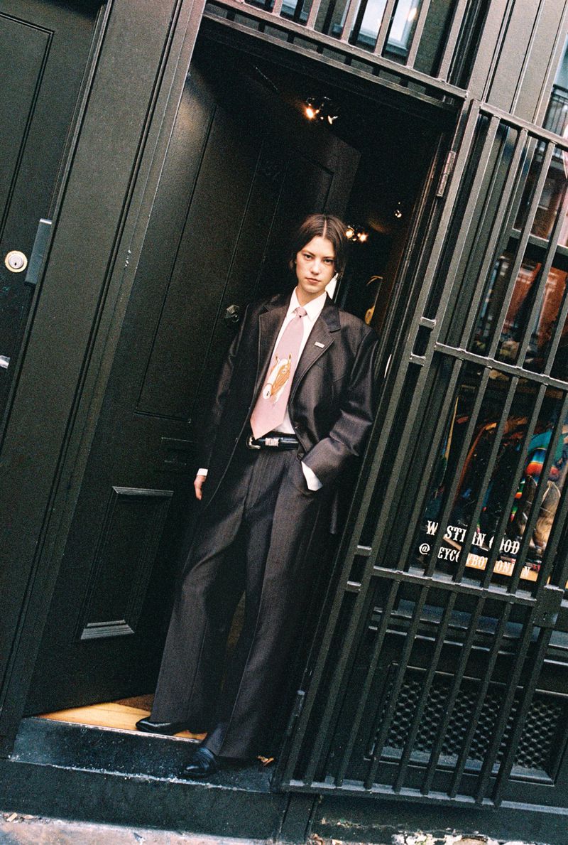 Model Dana Smith poses in an oversized dark tailored suit and wide pink tie in an urban doorway for i-D Magazine.