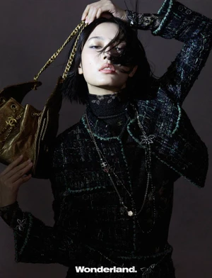 Model in dark patterned tweed jacket holding a gold chain handbag against a dark background for Wonderland China.
