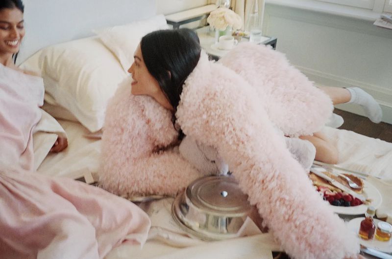 Models in a bright bedroom setting with breakfast trays, wearing fluffy pink textured apparel